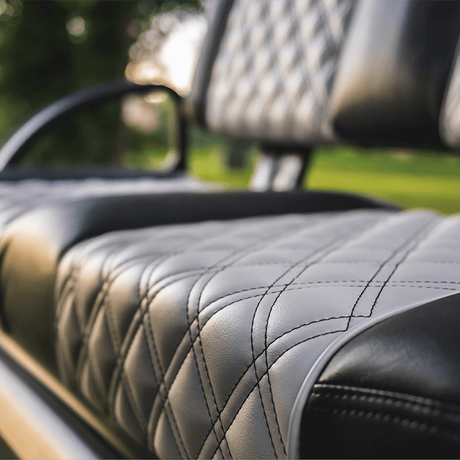 Close-up of a black and gray quilted leather seat with diamond stitching, showing the texture and upholstery details, with a blurred outdoor background.