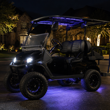 A black off-road utility cart or golf cart parked on a residential driveway at night, illuminated by white headlights and blue LED under-seat and roof lighting.