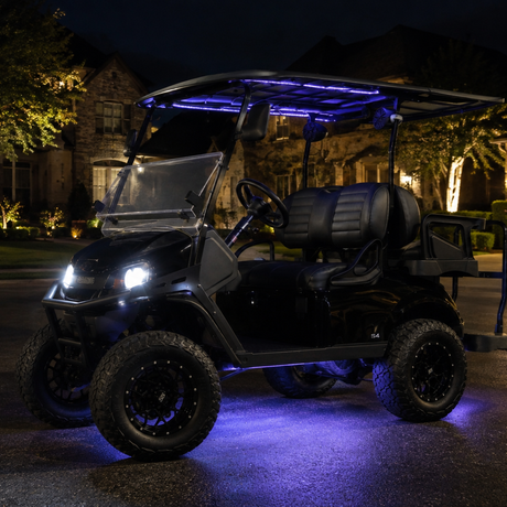 A black off-road utility cart or golf cart parked on a residential driveway at night, illuminated by white headlights and blue LED under-seat and roof lighting.