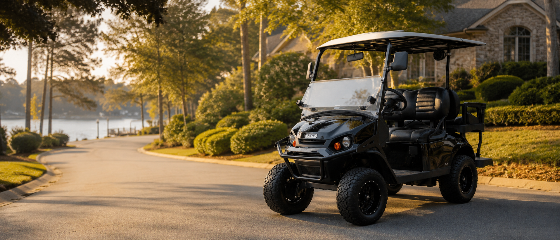 A black electric golf cart with a clear canopy and four wheels, parked on a paved path in a landscaped residential area with trees, shrubs, and a house in the background.